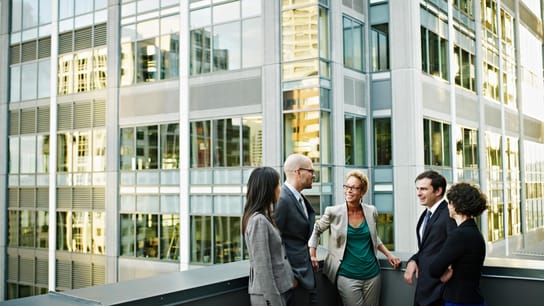 Boosting Trade and Collaboration Across the Commonwealth - Group of coworkers standing in discussion on deck of office buildings in background