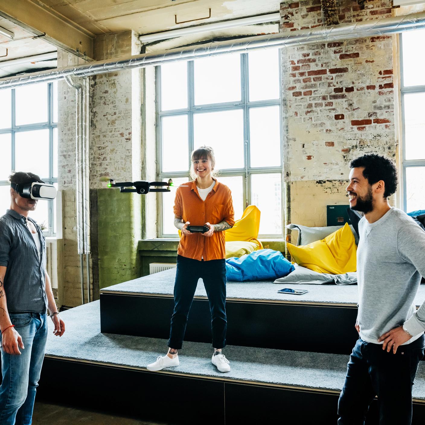 Jóvenes empresarios emergentes volando un drone dentro de una gran oficina. Un hombre que usa gafas de realidad virtual y prueba un nuevo software de realidad aumentada con la cámara del drone.
