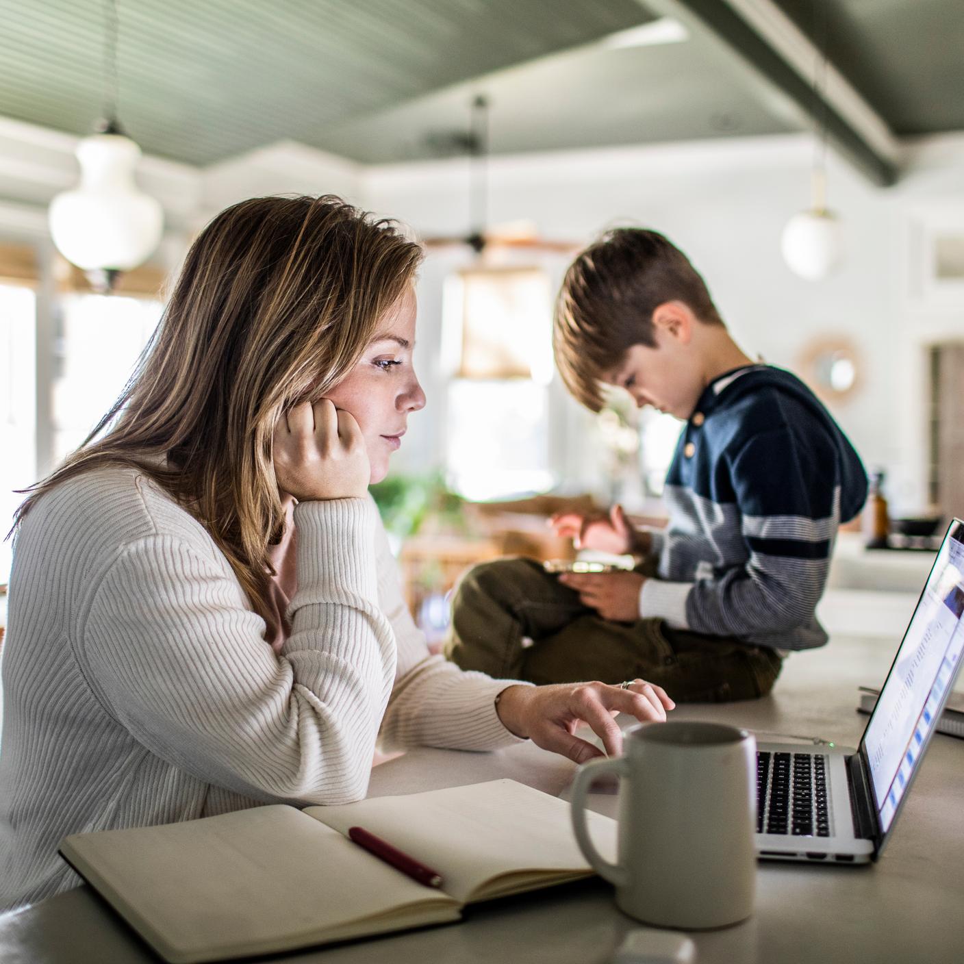 La certification Kitemark™ pour un service inclusif - Une femme travaille à domicile sur un ordinateur portable tandis que son fils utilise un téléphone intelligent