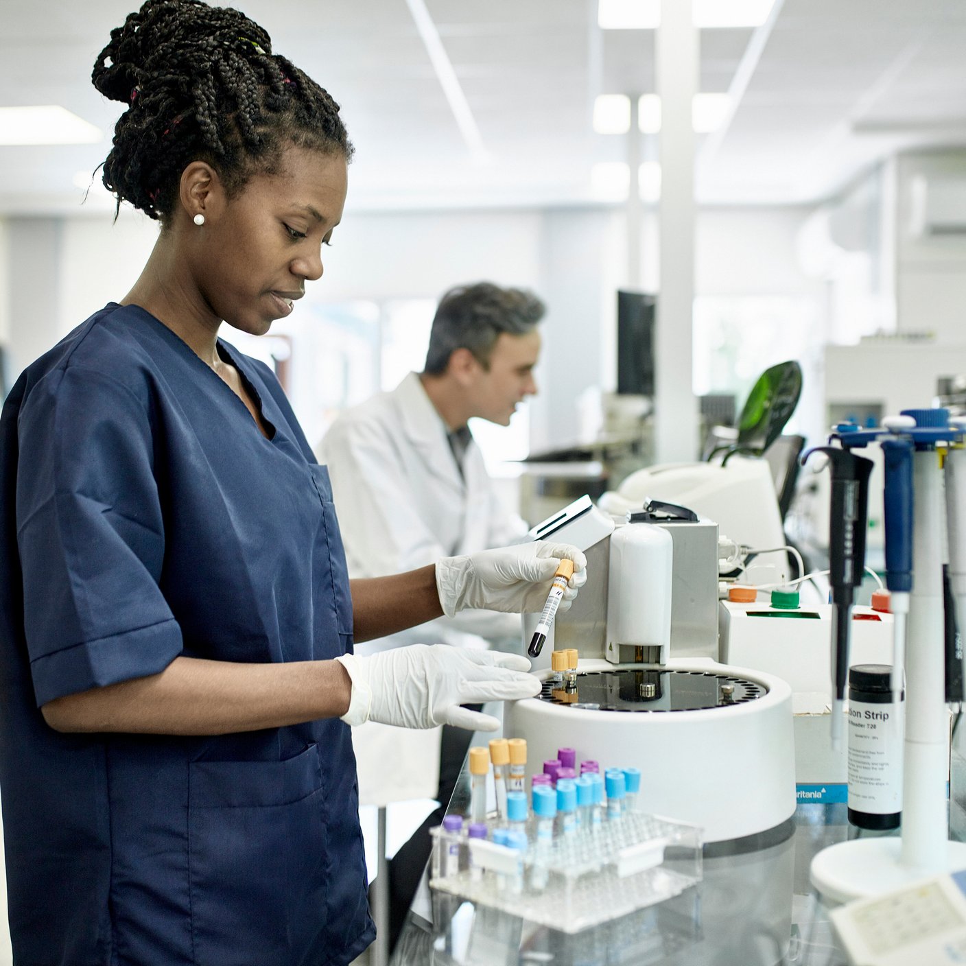 Smiling African female pathology technician in blue scrubs preparing test tubes for analysis in Buenos Aires clinical analysis laboratory.