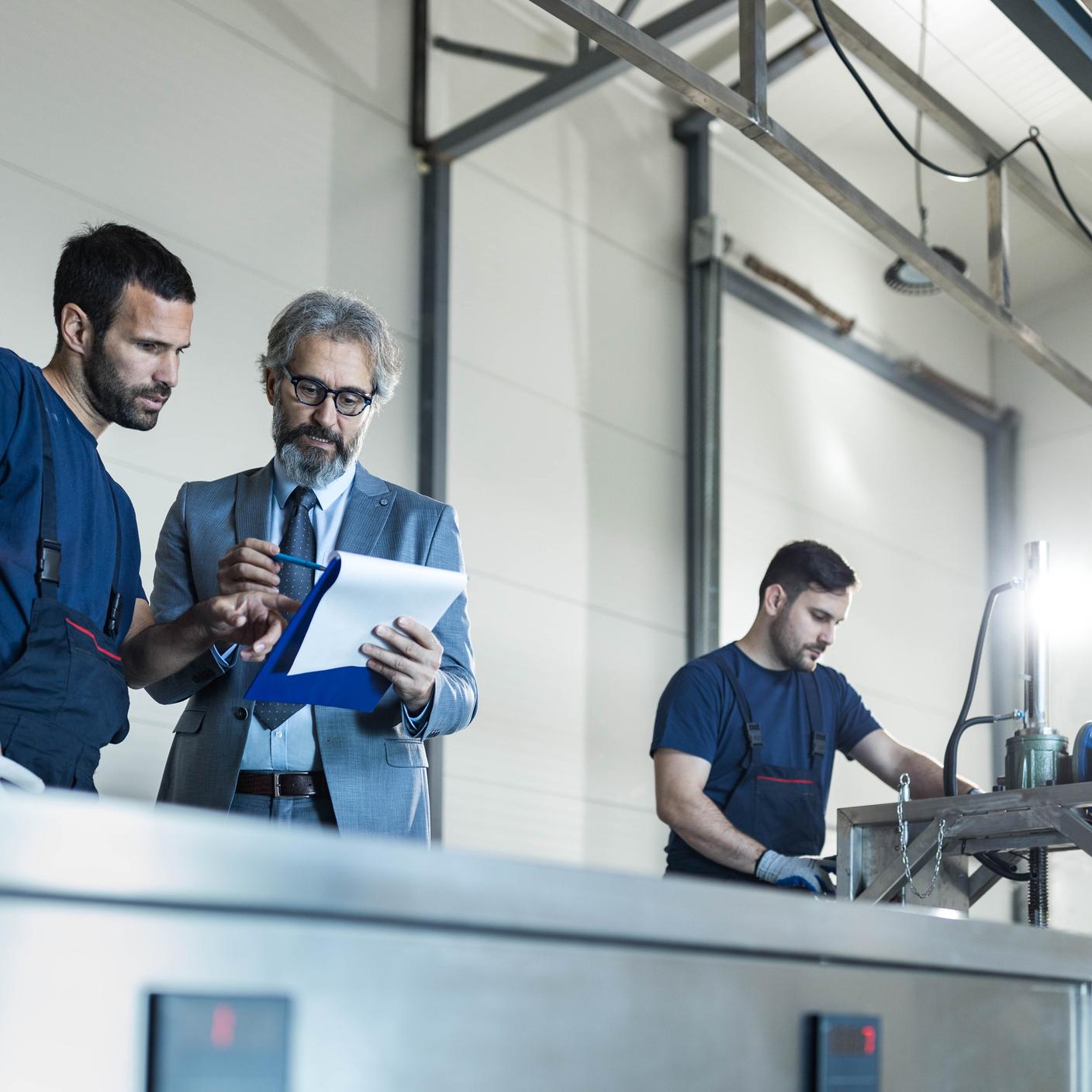 Mature inspector and manual worker going through paperwork in a factory. 