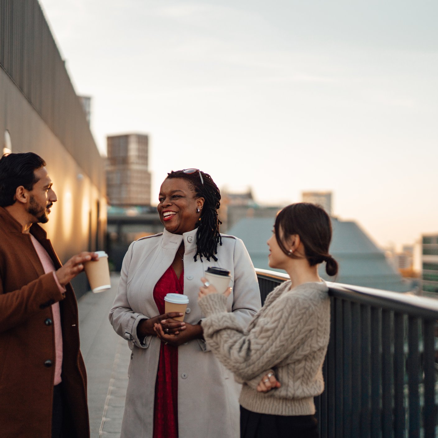 Cheerful multi-ethnic business people standing by railing at rooftop