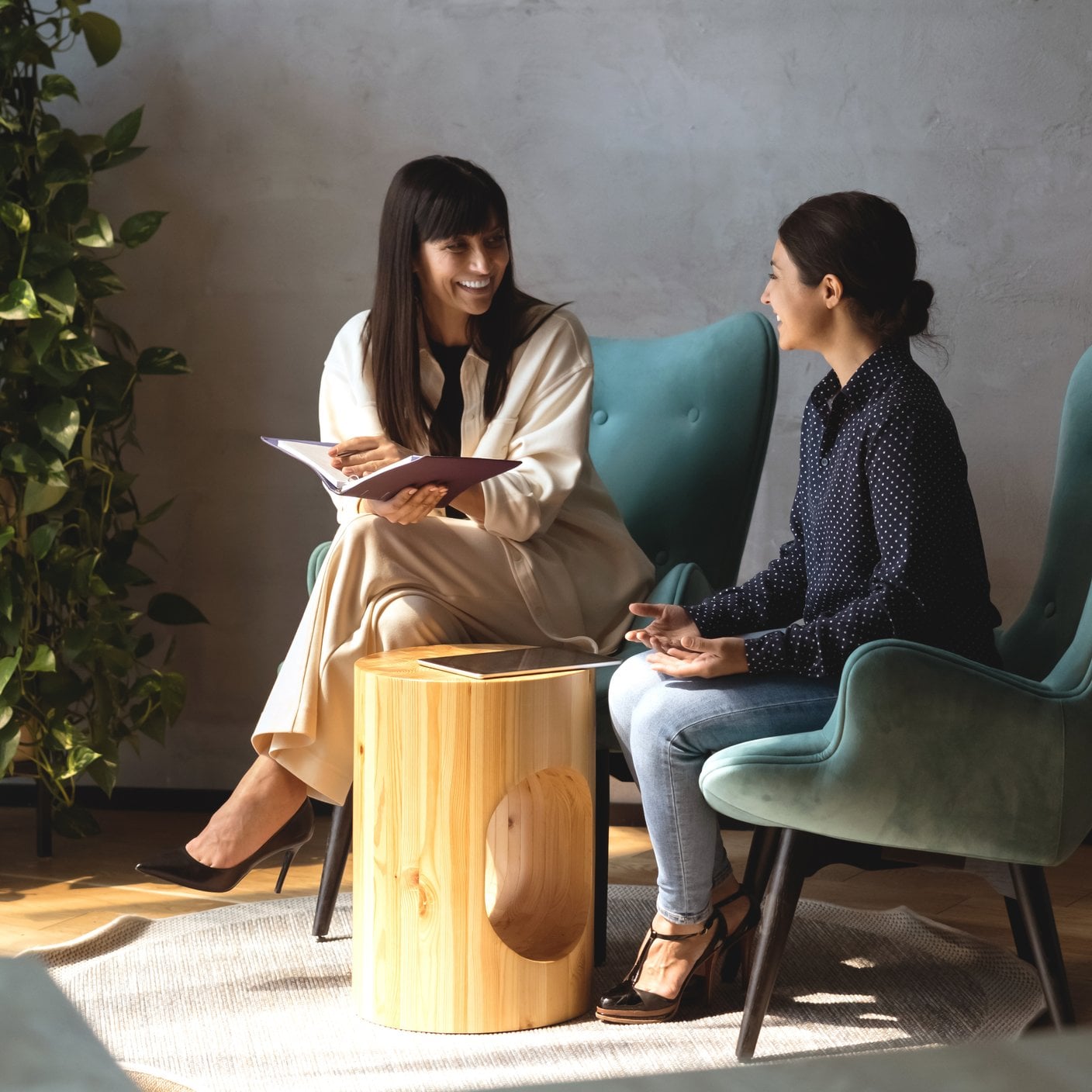 Duas colegas simpáticas, sentadas em poltronas, desfrutam de uma conversa agradável e compartilham informações em uma reunião informal no moderno saguão do escritório. Conversa entre empresárias indianas e caucasianas durante o fluxo de trabalho (cortado)
