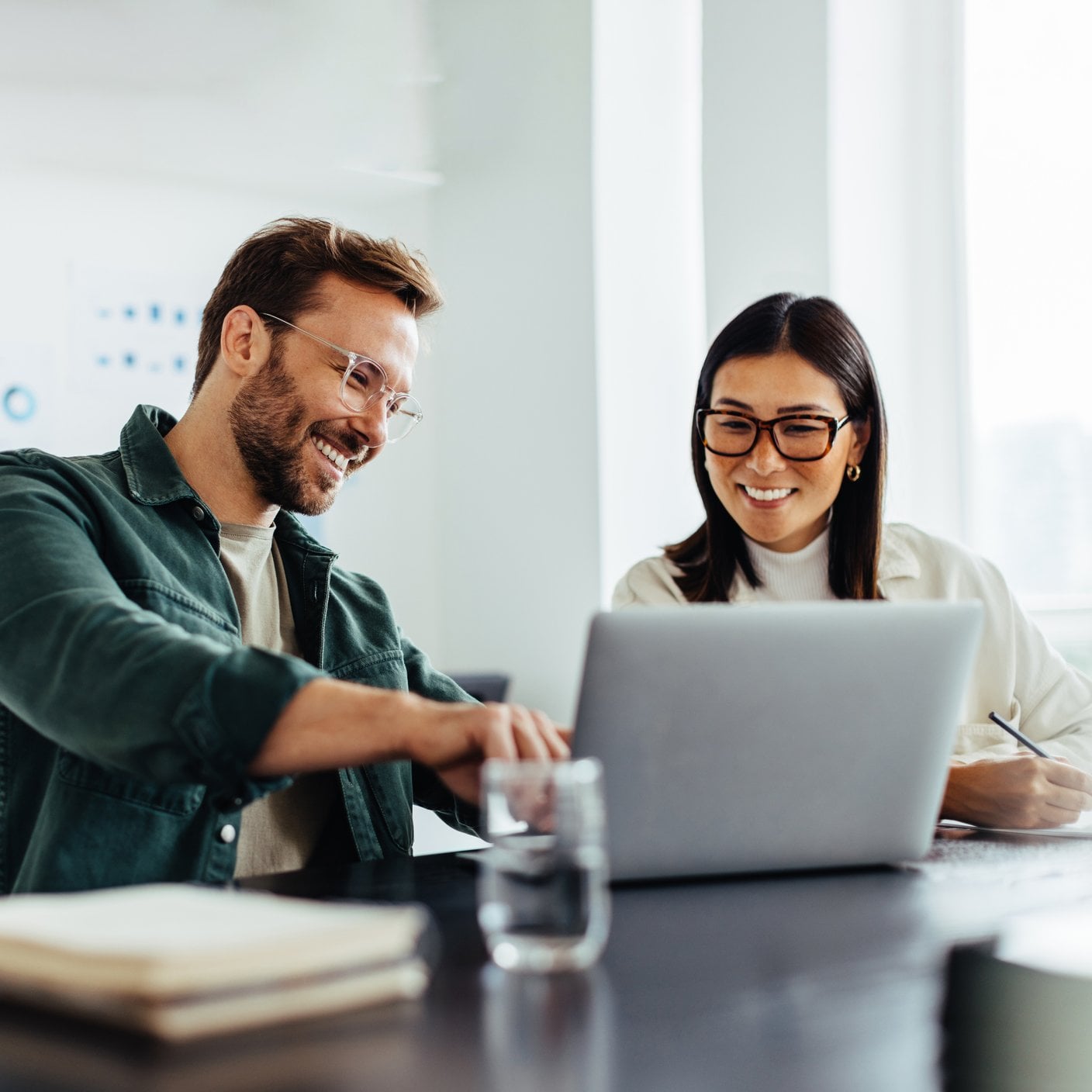 A man and a woman sat at a desk looking at a laptop