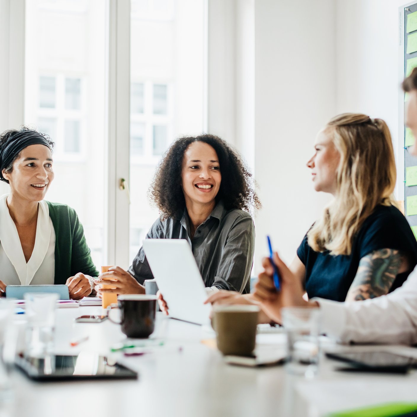 A group of office workers sitting down and talking together at a large desk during a morning meeting.