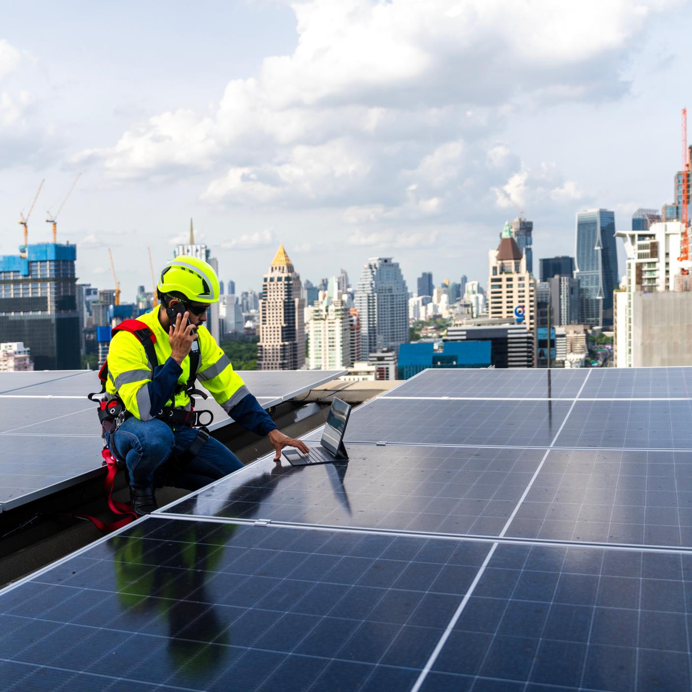 An engineer in protective gear examines solar panels on a rooftop, with a city skyline in the background, highlighting renewable energy in urban settings.