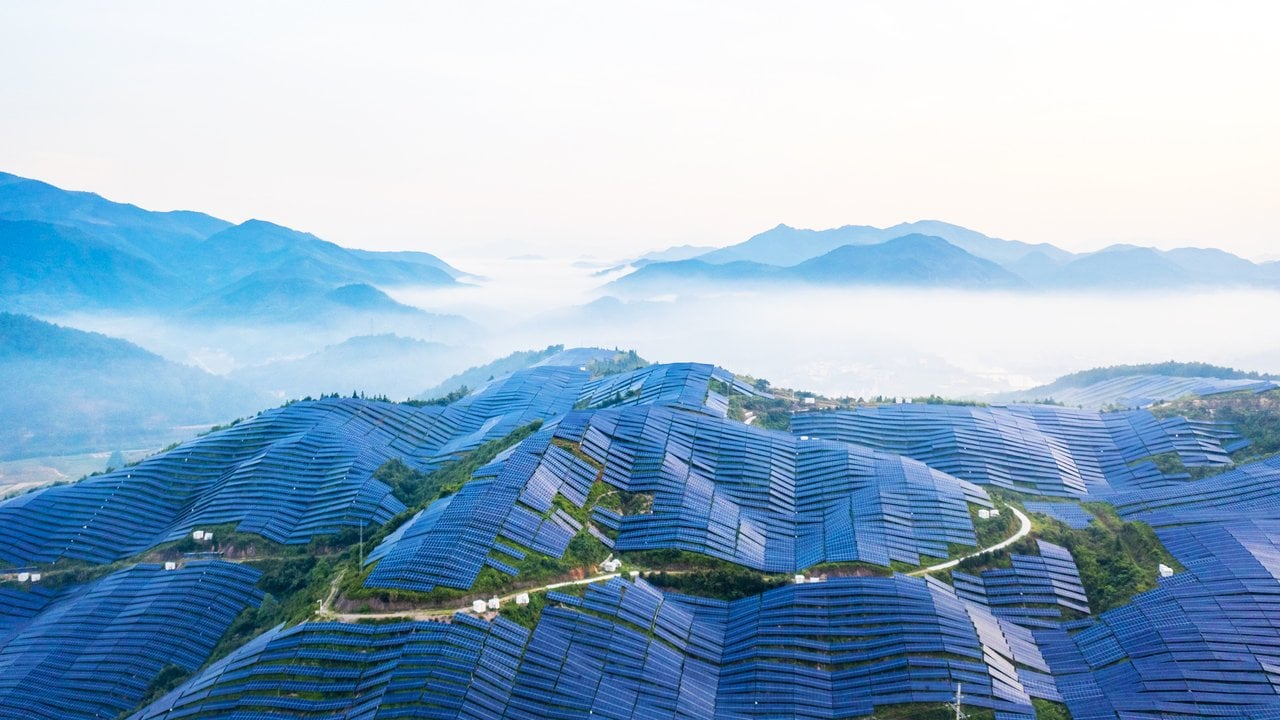 Solar panels covering rolling green hills, with misty mountains in the background.