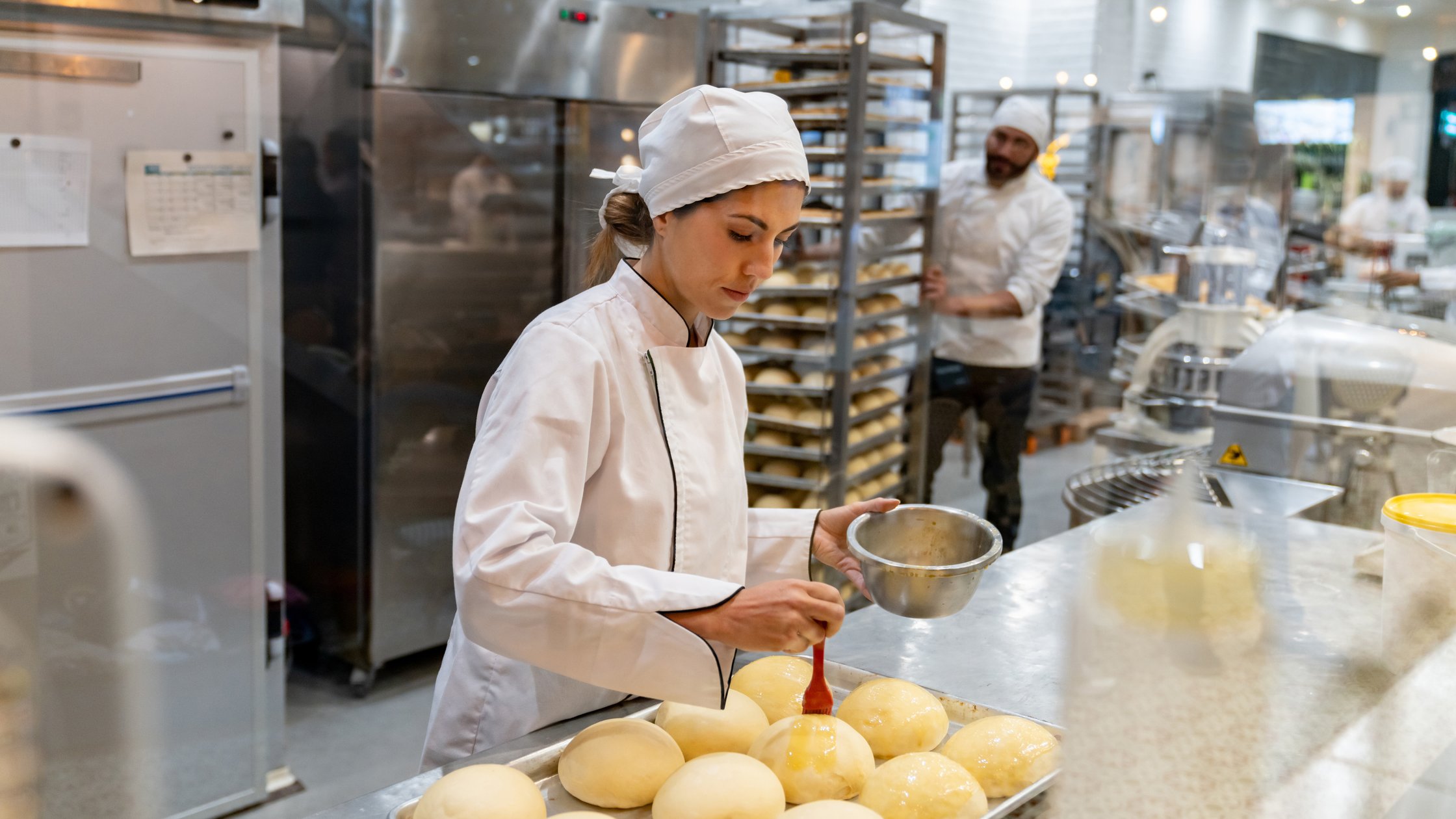 Female baker spreading egg yolks on bread while baking at the bakery.