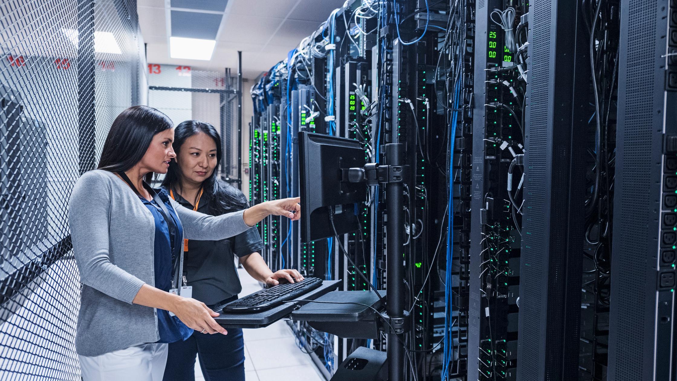 Two female operators in a large data centre making checks on servers